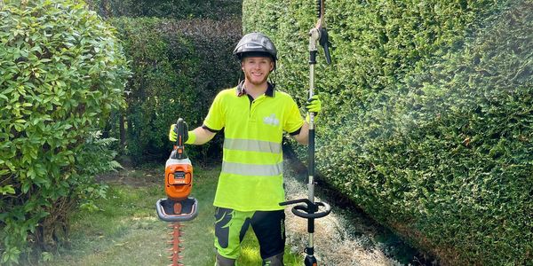 Gardener in neon attire holding hedge trimmers in a lush garden.