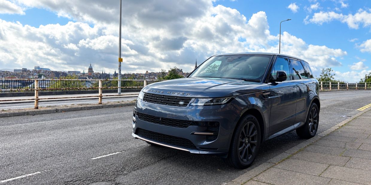 A blue Range Rover parked on a street with a cloudy sky.