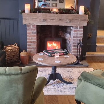 Cozy living room with green chairs, a leather sofa, and a warm fireplace.