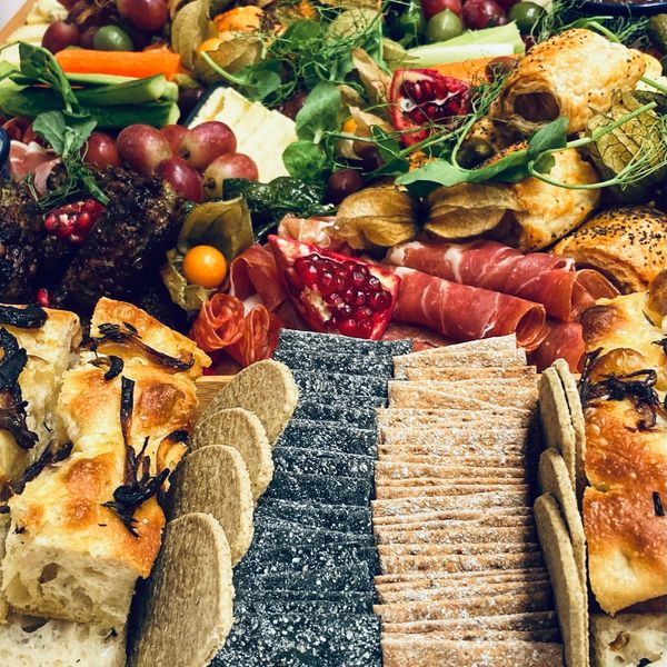 A grazing boards of focaccia, cheeses, charcuters, pomegranate, grapses, crudites, sausage rolls.