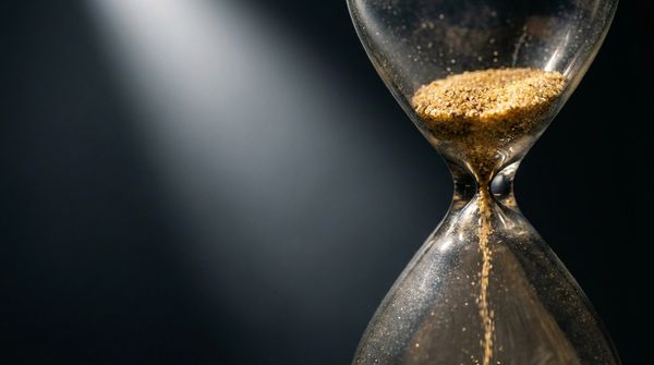 Close-up of an hourglass with sand running through it against a dark background.