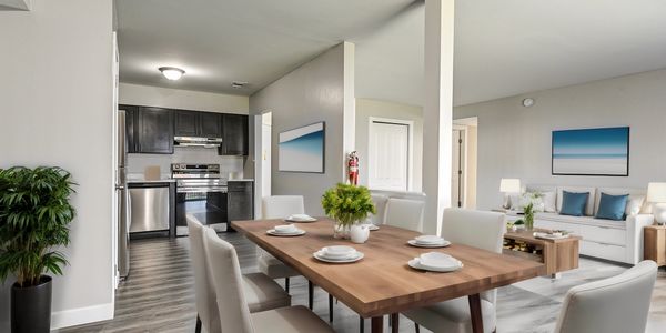 Modern dining area with wooden table and white chairs adjacent to kitchen and living room.