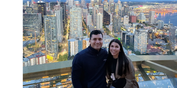 Couple posing with a city skyline at dusk from a high viewpoint.