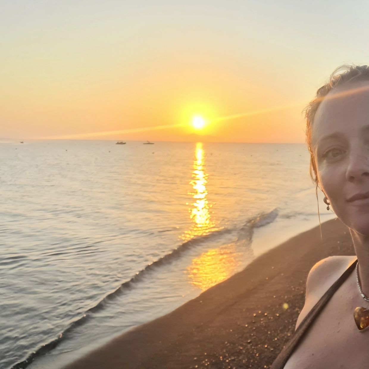 Woman taking selfie on a beach during a golden sunset with calm waves.