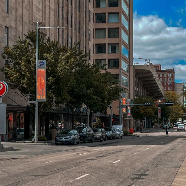 Urban street scene with parked cars and tall buildings under a blue sky.