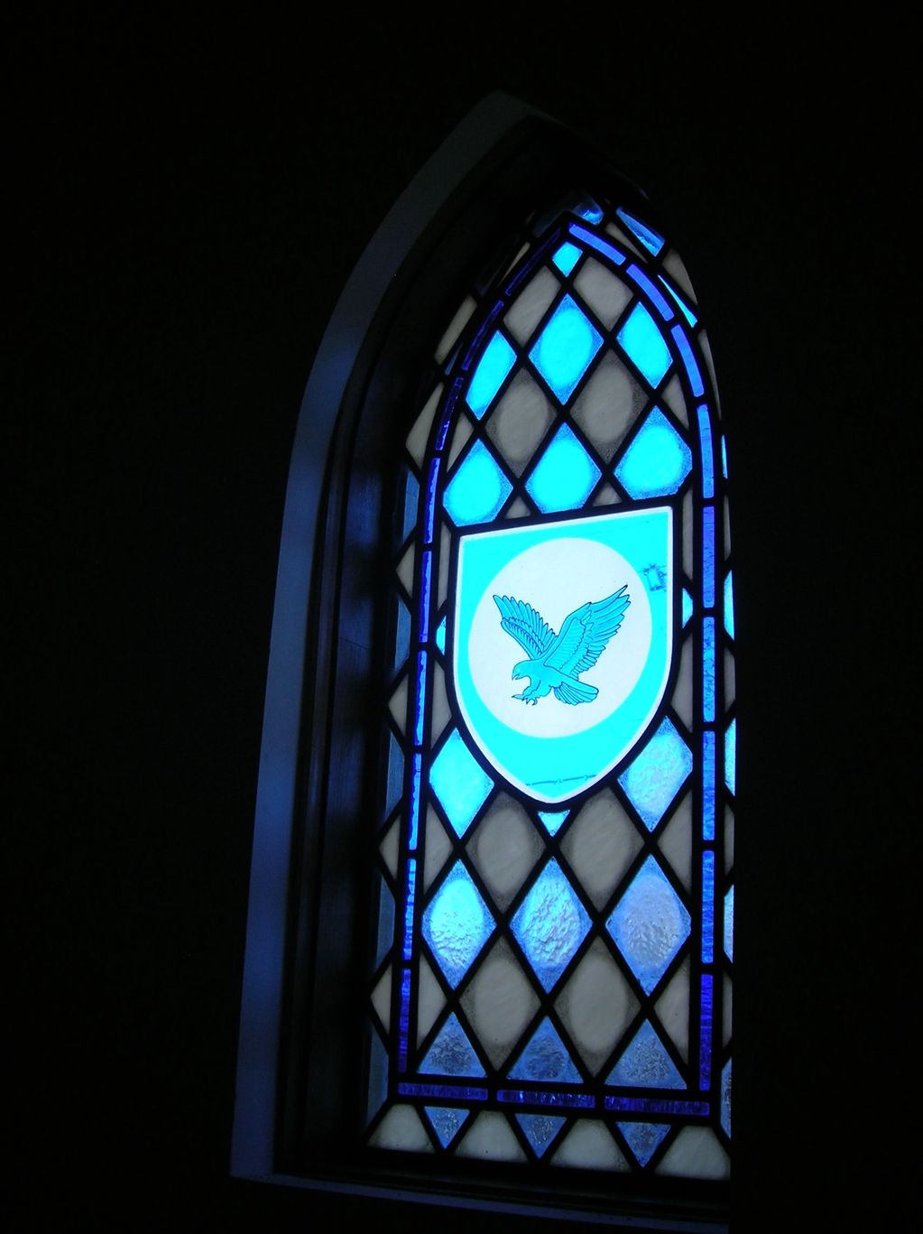 Blue bird flying in front of moon in sigil in center of stained glass window