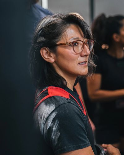 A woman with glasses and chalk on her shoulder looks focused.