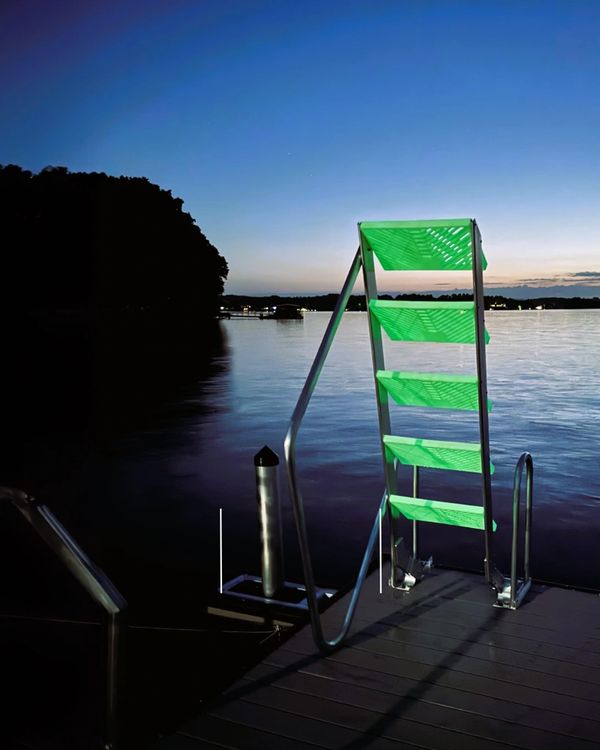 Green ladder on a dock leading into calm water at twilight.