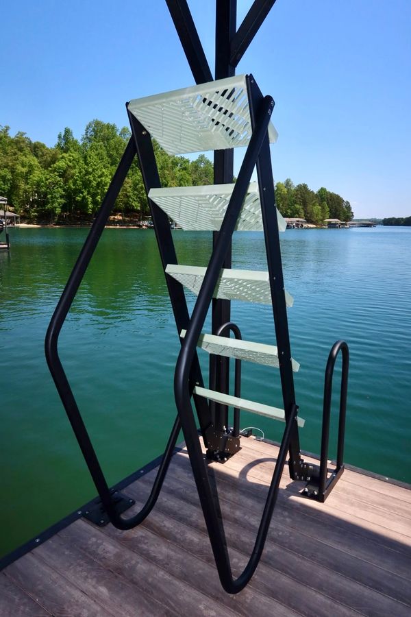 Modern metal ladder on a lakeside dock under clear blue sky.