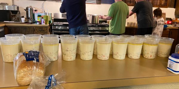 Row of cups filled with creamy dessert on a counter with people cooking in the background.