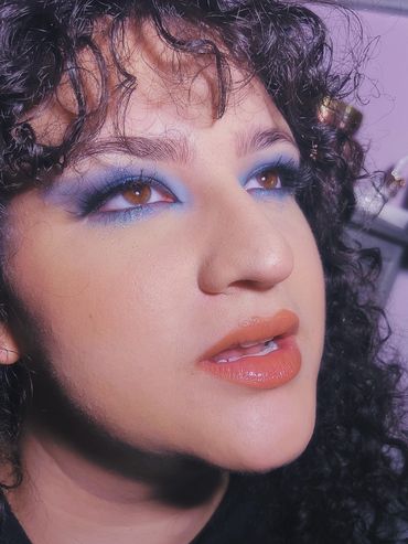 Close-up of a person with curly hair and vibrant blue eyeshadow.