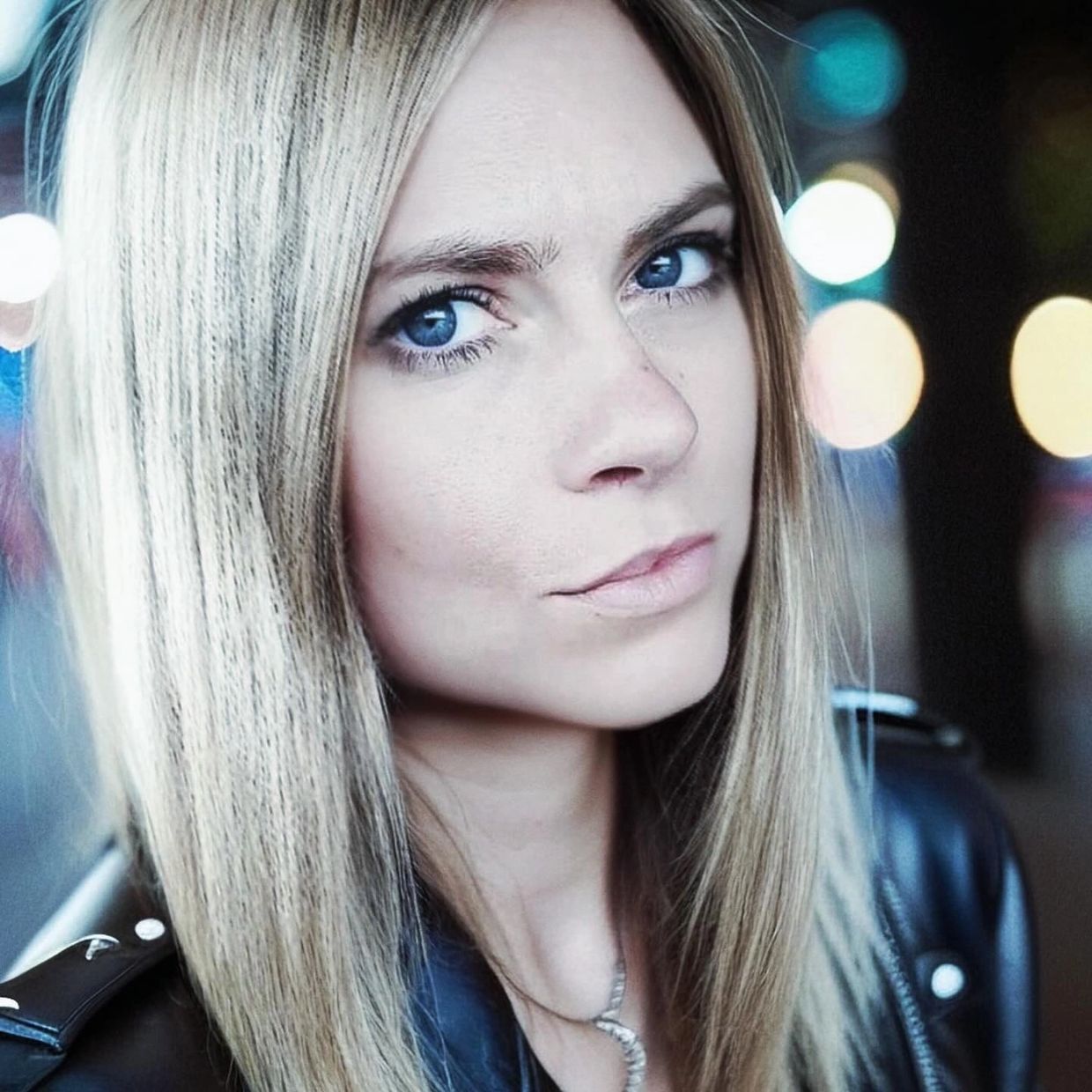 Close-up of a woman with blonde hair and blue eyes wearing a black leather jacket. Its Hannah Bellmann.