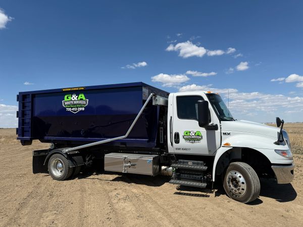 Truck with a purple roll off dumpster. On a flat dirt land.
