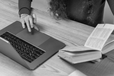 Se muestra a una mujer trabajando con computadora y un libro