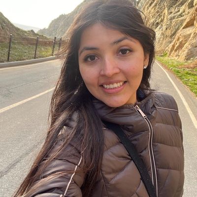 Smiling woman in a brown jacket taking a selfie outdoors.