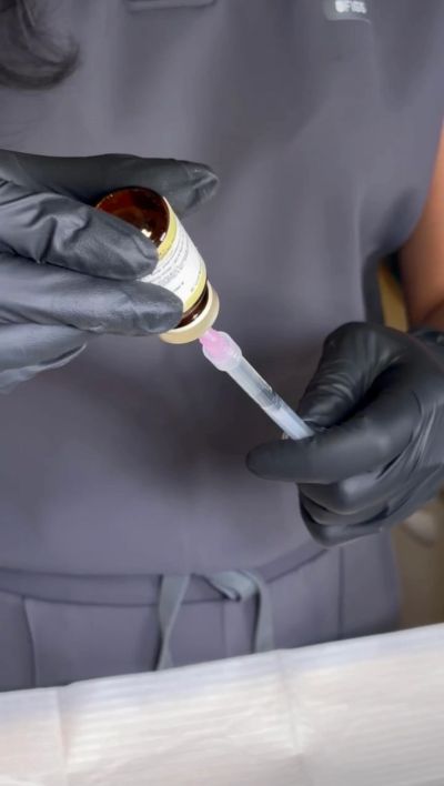 Hands in black gloves handling a vaccine syringe.