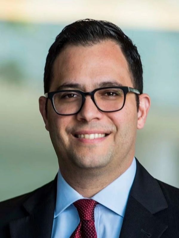 Smiling man wearing glasses, suit, and red tie.