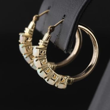 Gold hoop earrings with opal stones on a black display.