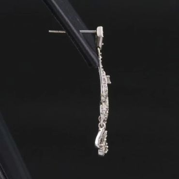 Silver saxophone-shaped earring held by tweezers.