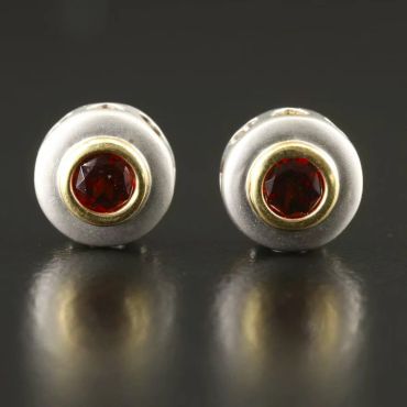Pair of round white and yellow gold earrings with ruby gemstone centers.