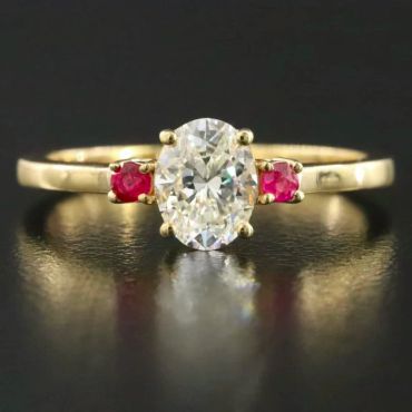 Gold ring with an oval diamond and two red stones.