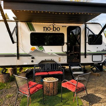 Outdoor seating area with red cushions in front of a No Bo camper trailer.