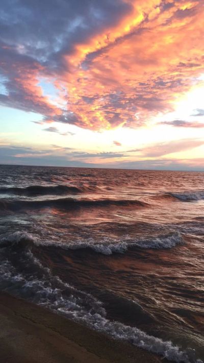 Sunset sky with vibrant orange clouds over a wavy sea.