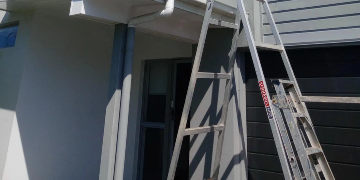 Modern house exterior with ladders against white and gray walls.
