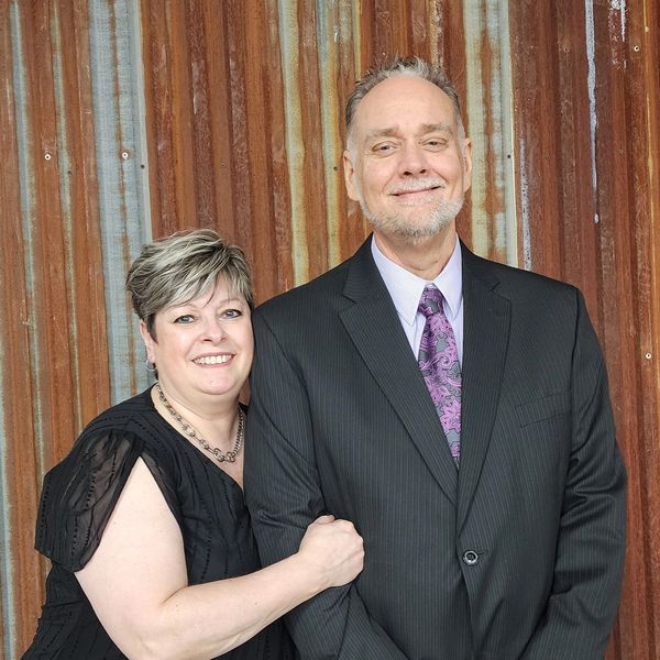 Smiling couple posing together against a rustic corrugated metal wall.