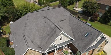Aerial view of a large house with a complex gray roof and surrounding greenery.