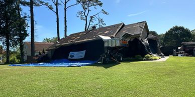 A house severely damaged by a storm with a tarp covering parts of the roof.