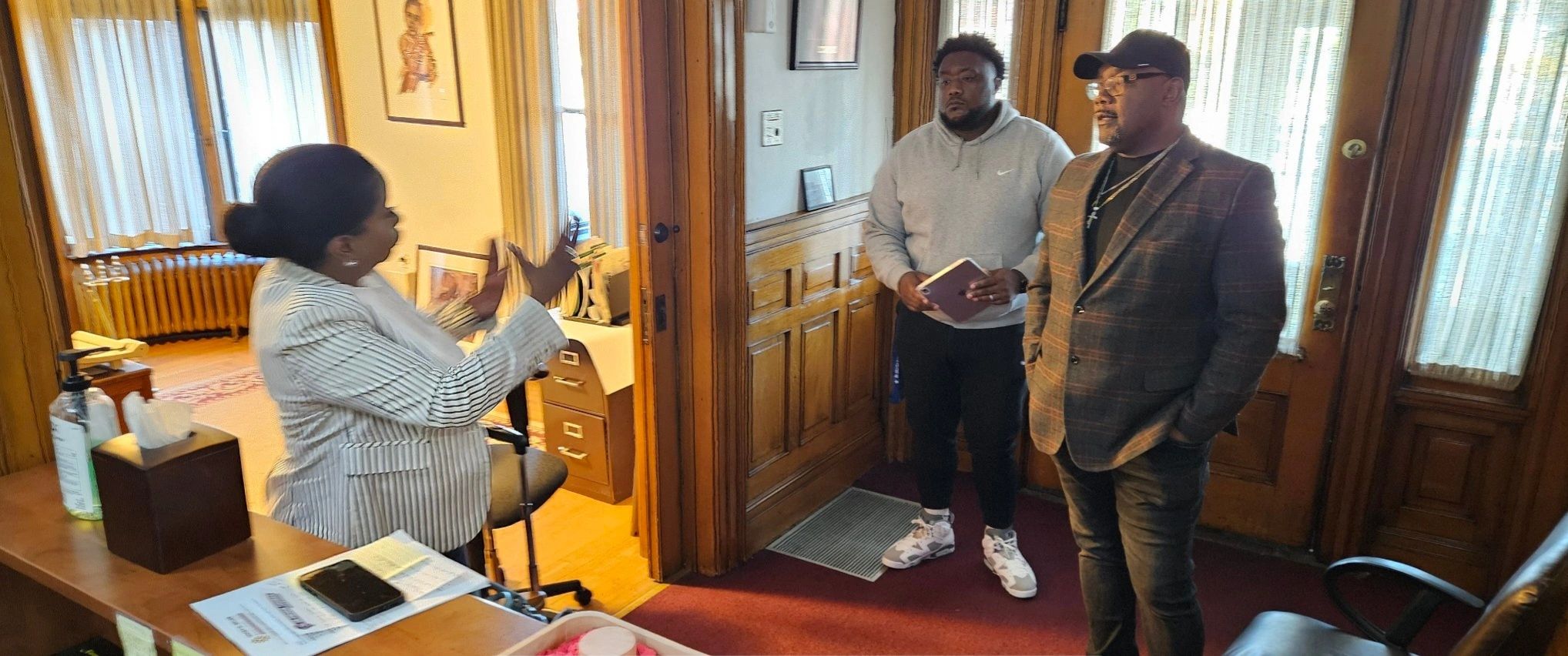 A woman speaks animatedly to two men in an office setting.