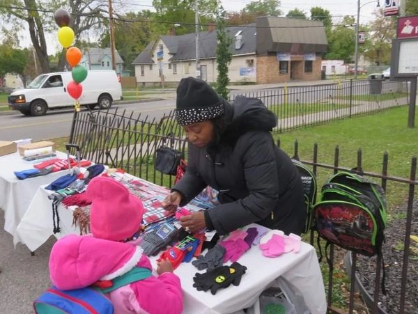 A woman helps a child pick winter gloves at an outdoor table.