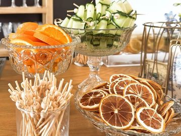 Glass bowls with fresh and dried citrus slices and cucumber skewers on a wooden table.