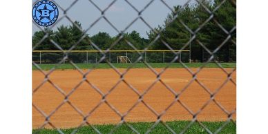 Baseball field viewed through a chain-link fence on a sunny day.