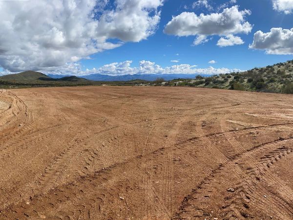 Cleared dirt area with tire tracks under a partly cloudy sky and distant hills.