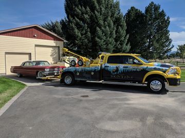 tow truck with classic car attached sits in driveway