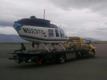 yellow tow truck hauls broken helicopter