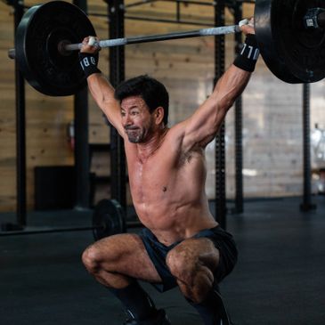 Man performing overhead squat with heavy barbell in gym.
