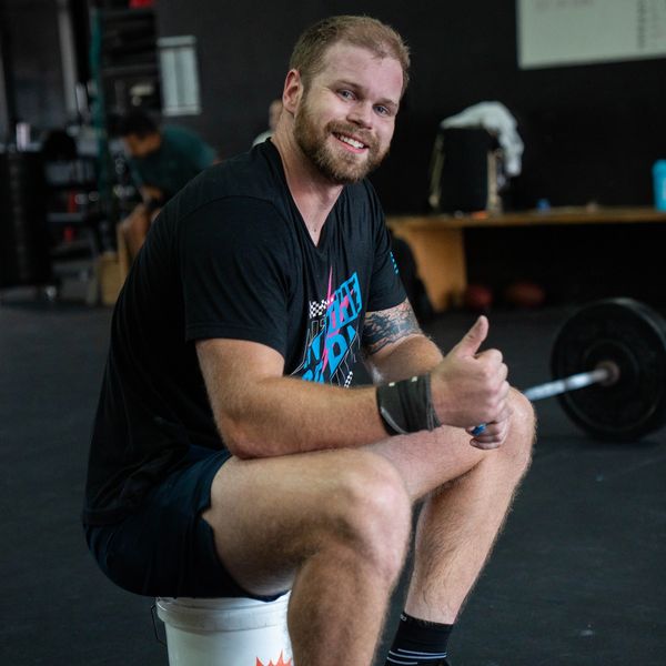 Smiling man sitting on a bucket in a gym giving a thumbs up.