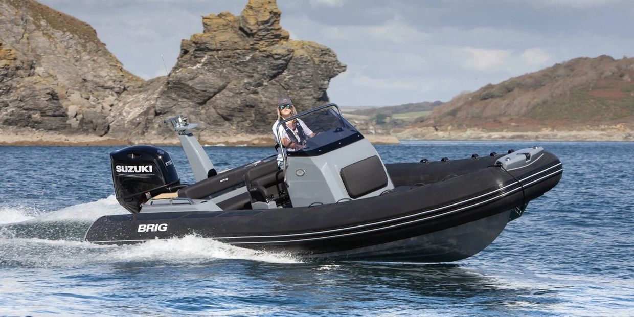 A person driving a black and gray BRIG speedboat on the water near rocky shores.