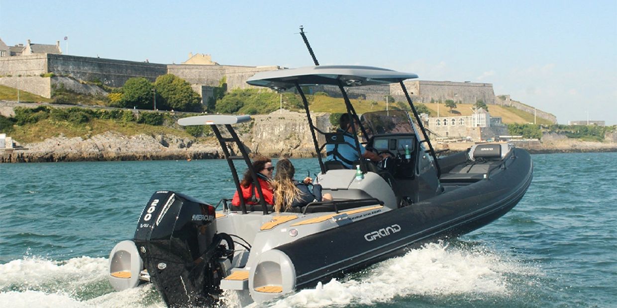 A motorboat with people cruising near a coastal fortress on a sunny day.