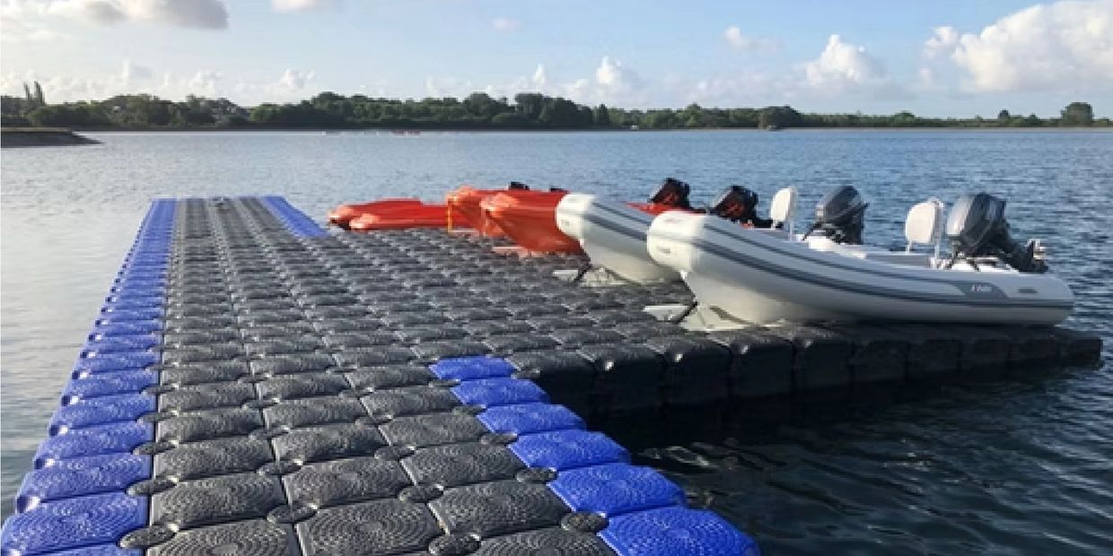 Boats docked on a floating modular dock in a calm lake under a blue sky.