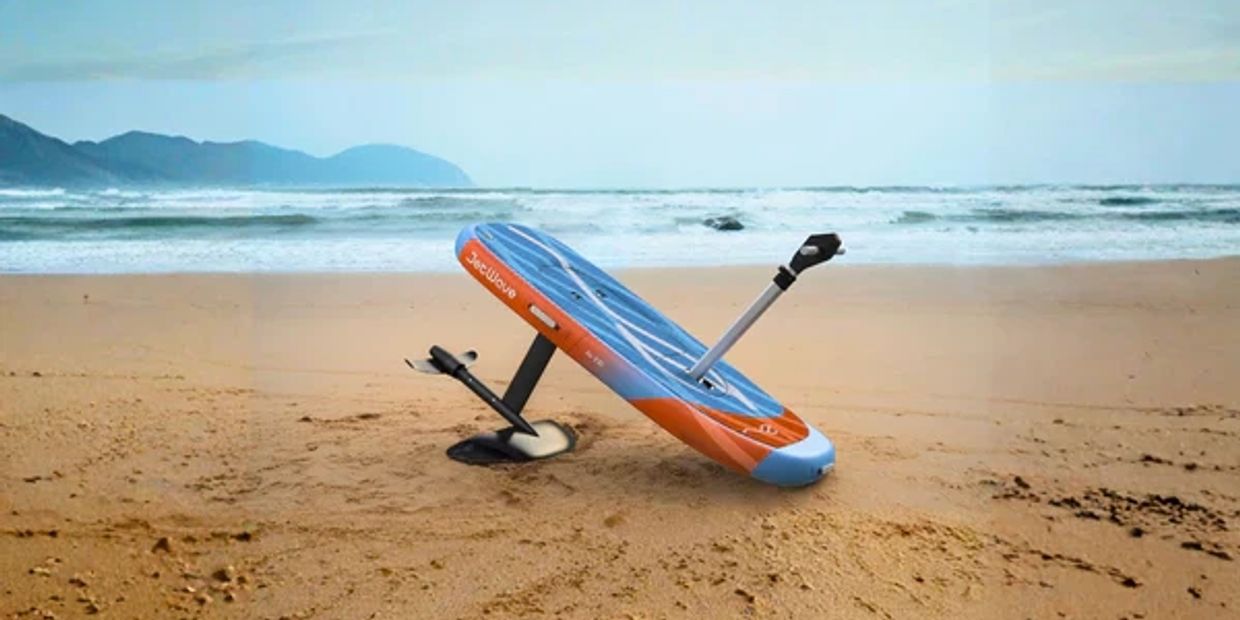 A hydrofoil surfboard resting on a sandy beach near the ocean.