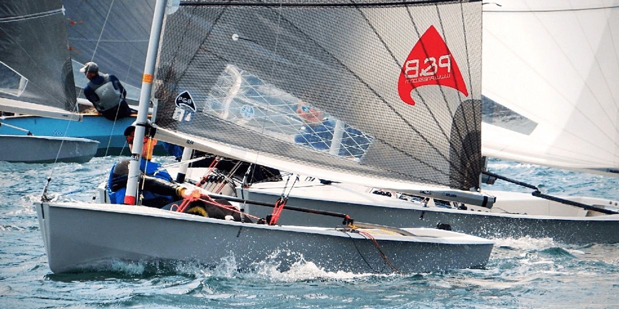 Two sailboats racing closely on the water with sailors maneuvering.