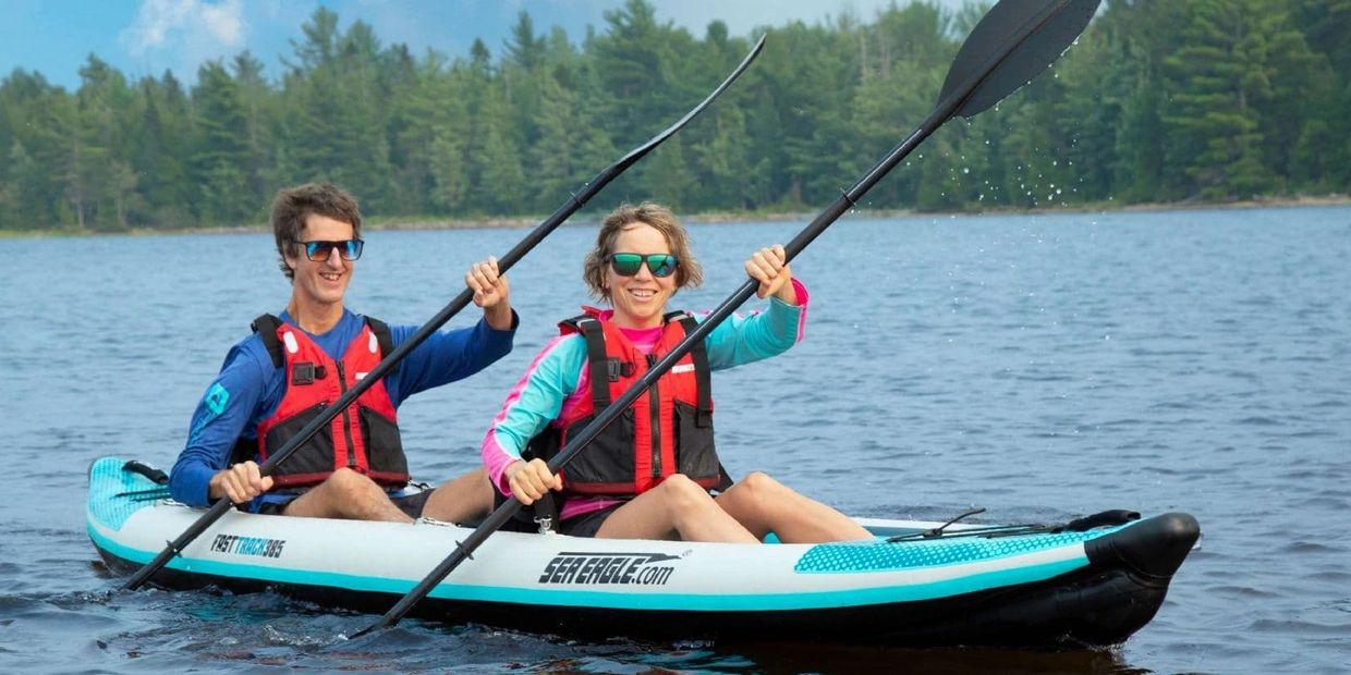 Two people kayaking on a lake wearing life jackets and sunglasses.