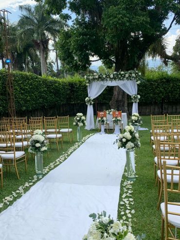 Outdoor wedding aisle decorated with white flowers and golden chairs.