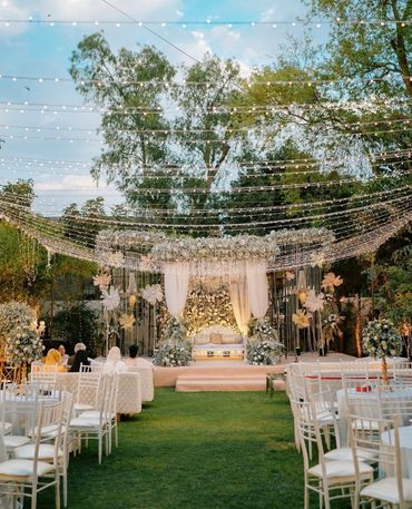Elegant outdoor wedding setup with floral decorations and string lights.