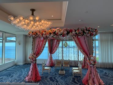 Elegant floral wedding mandap with ocean view in a decorated indoor space.