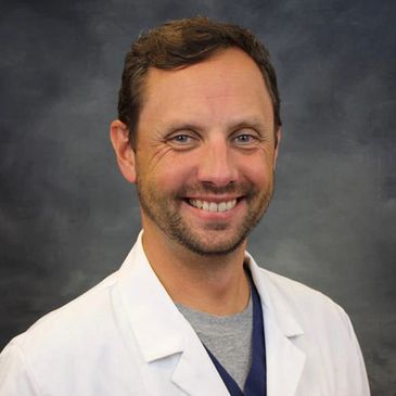 Smiling man in a white lab coat against a dark background.